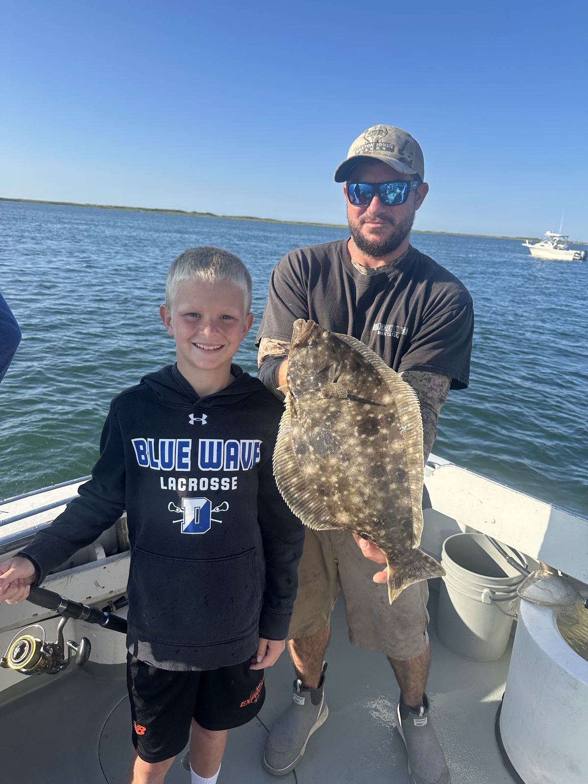 Captain Travis and a young angler holding a large fluke aboard the boat