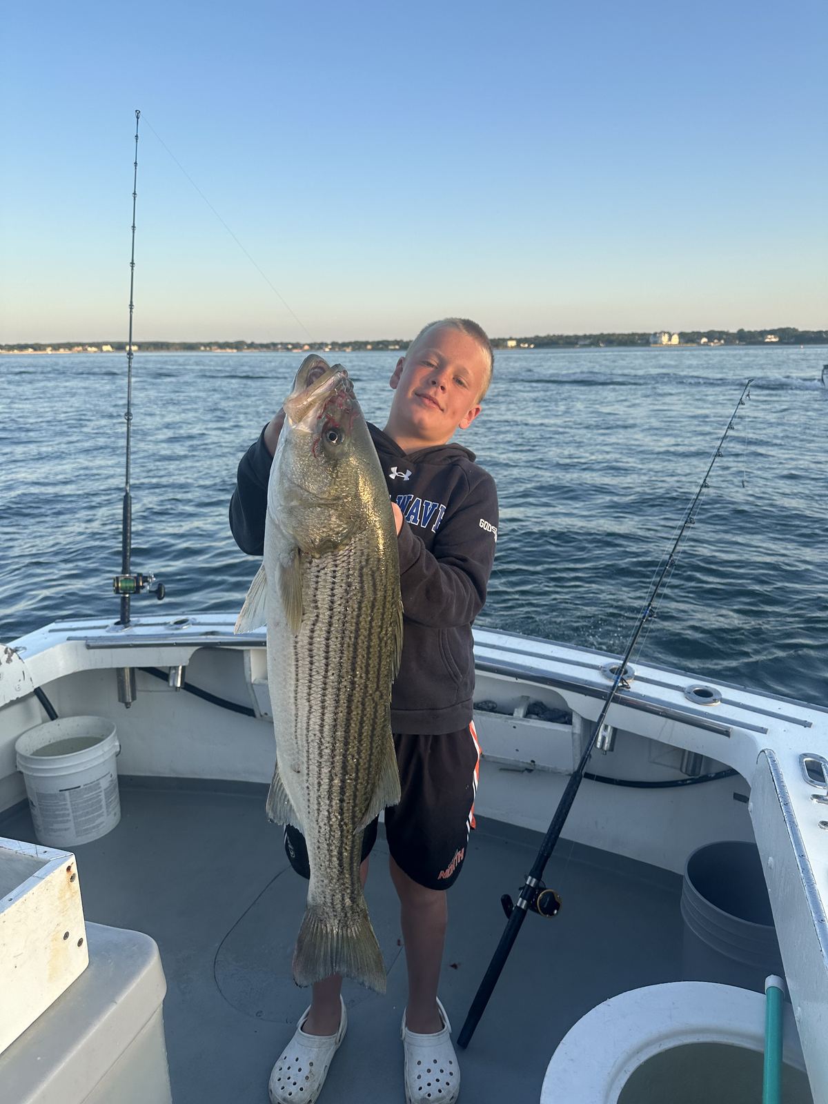 A young angler on the boat holding a large striped bass at dusk
