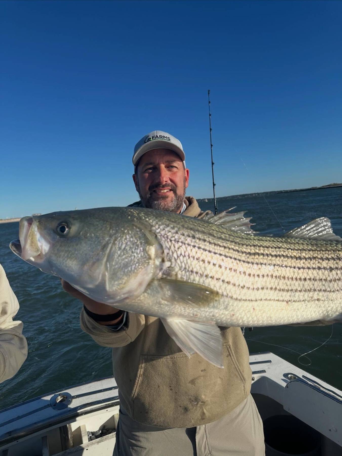 An adult angler presenting a large striped bass close to the camera on open water