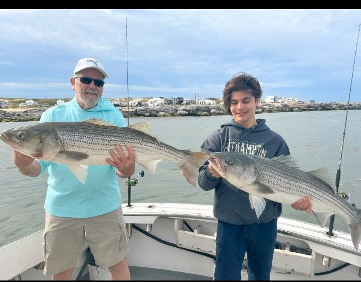 Two anglers side by side, each holding a striped bass aboard the boat