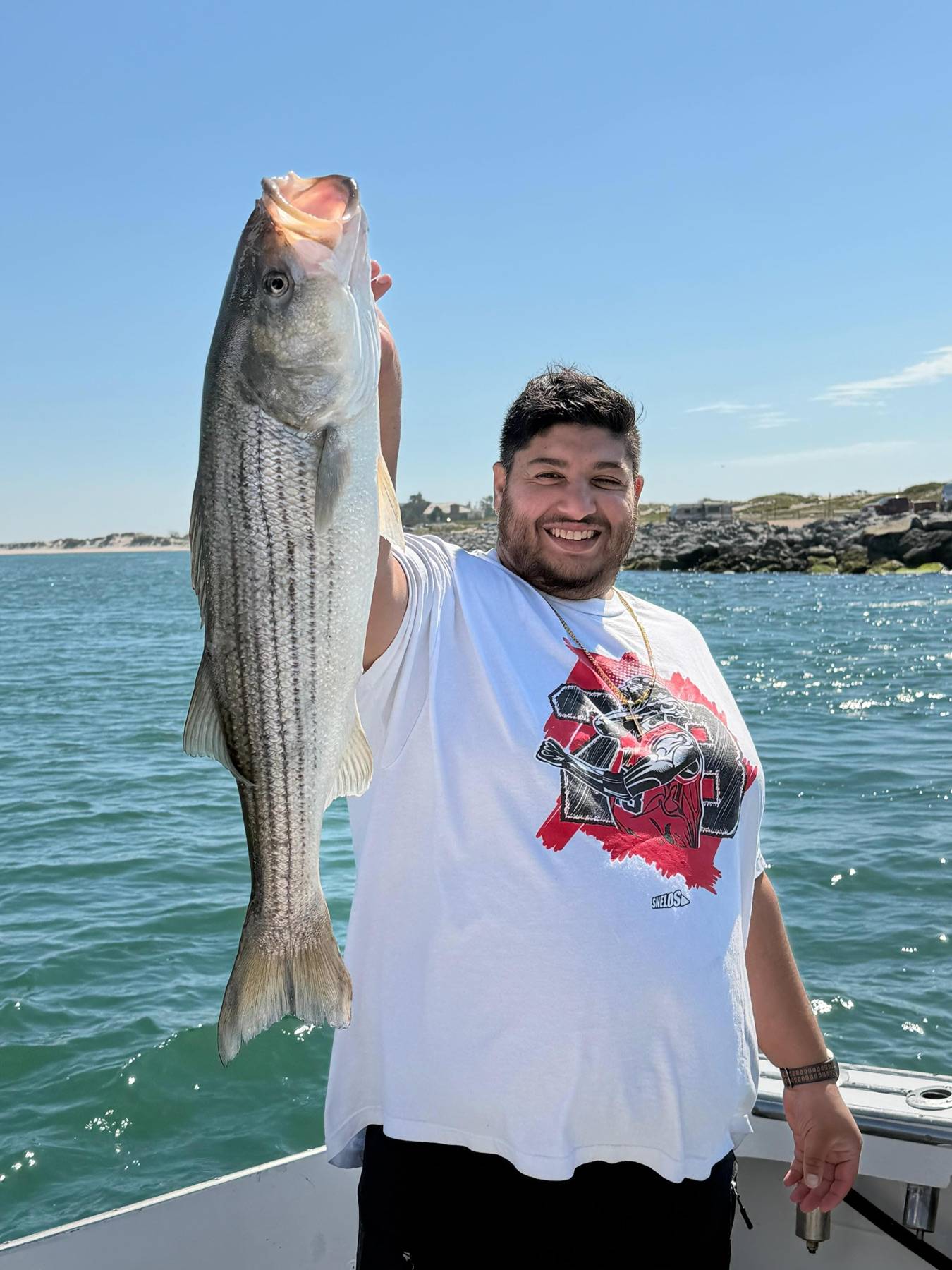 An adult angler smiling and holding a striped bass on bright blue water
