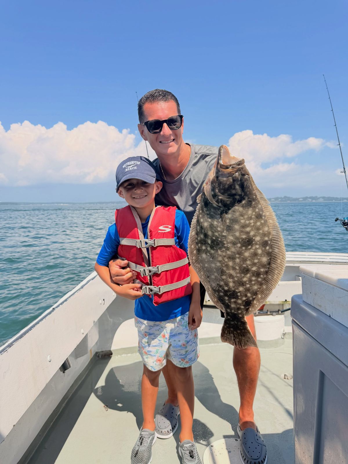 An adult and a child in a life vest holding a large fluke on the boat deck